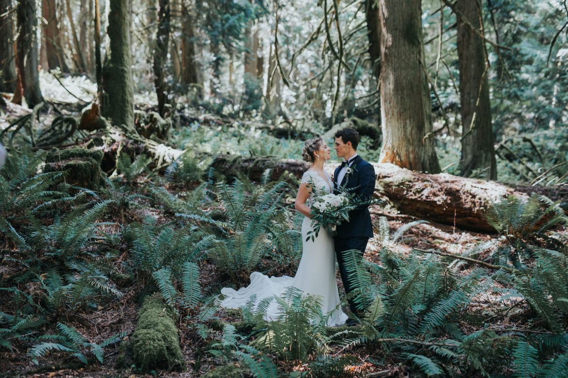 Couple posing during a romantic wedding photoshoot in a serene forest setting, surrounded by towering trees and natural greenery on Galiano Island.